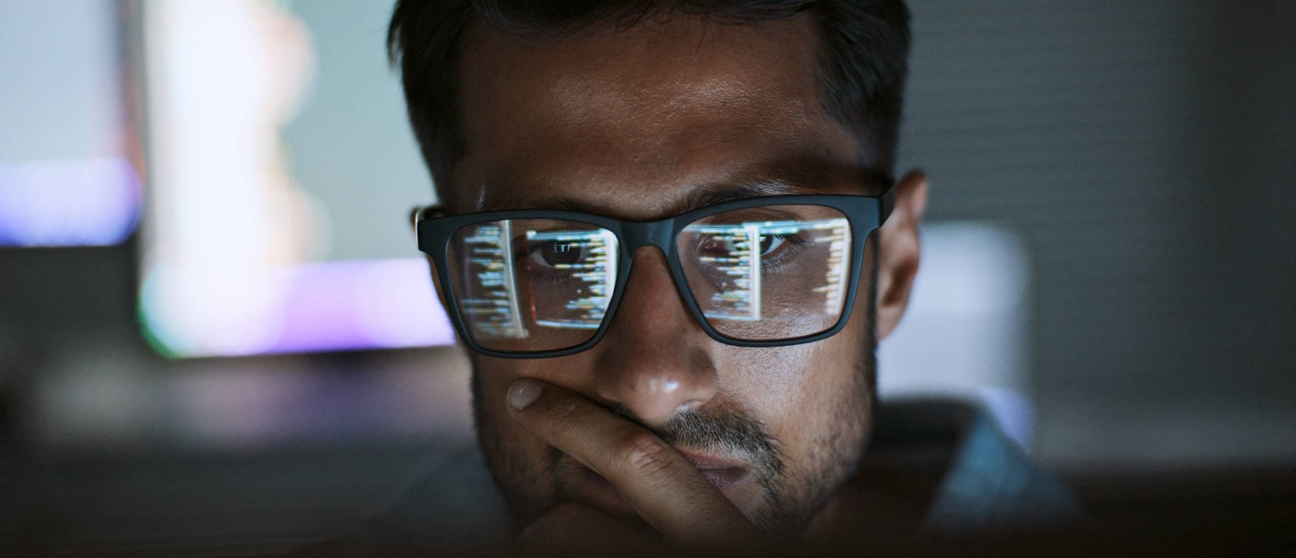 A man reviews analytics, with the screen reflecting in his glasses.
