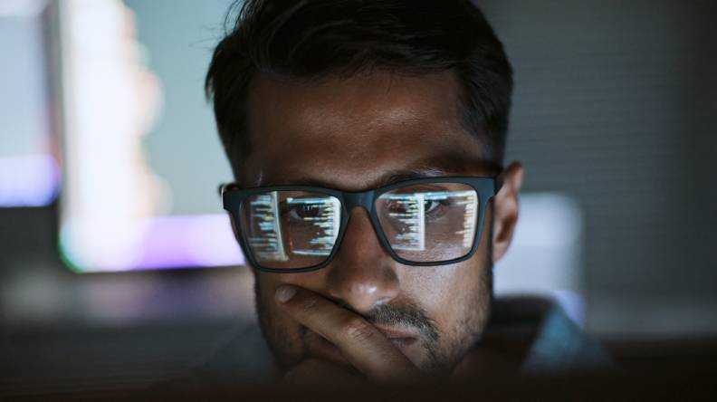 A man reviews analytics, with the screen reflecting in his glasses.